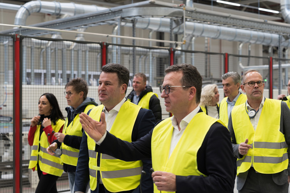 Alt-Text: „Fachleute in gelben Sicherheitswesten inspizieren eine industrielle Anlage für Sanitär- und Heiztechnik, umgeben von komplexem Rohrleitungs- und Maschinenapparat. - © Puris Bad