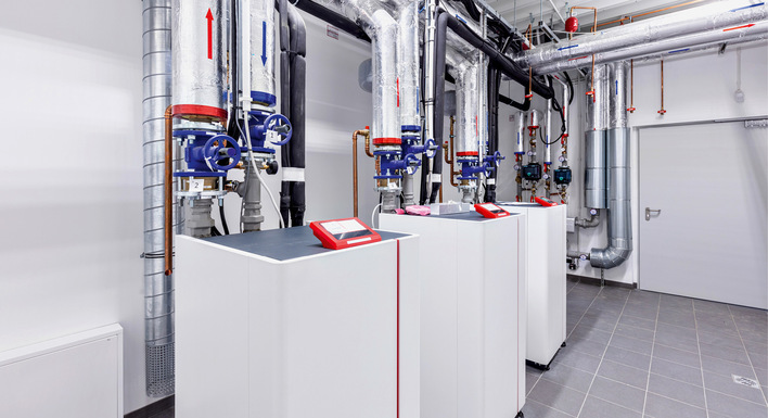 Drei Industriekessel mit Metallrohren und Schalttafeln in einem sauberen, modernen Technikraum. - © Bild: Mywarm / Getty Images