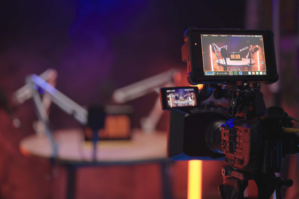 Eine Kamera filmt ein Podcast-Studio mit Mikrofonen und einem "On Air"-Schild auf einem runden Tisch. - © Video_StockOrg - stock.adobe.com