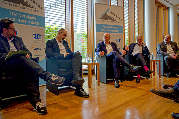 Fünf Männer in Geschäftskleidung sitzen auf Stühlen und diskutieren in einem hellen Konferenzraum. - © Kristian Barthen